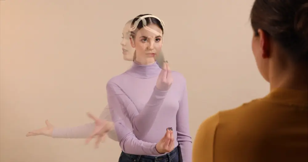 An overlay photo of a young woman wearing a futuristic hearing aid
        that spans over her head. She is interacting with the hearing aid
        through an expressive hand gesture, indicated through overlaid photos
        that represent a movement. She reaches out to a fictional disturbing
        noise, grabs the hearing focus of the interactive hearing aid, and sets
        it to her conversation partner.
